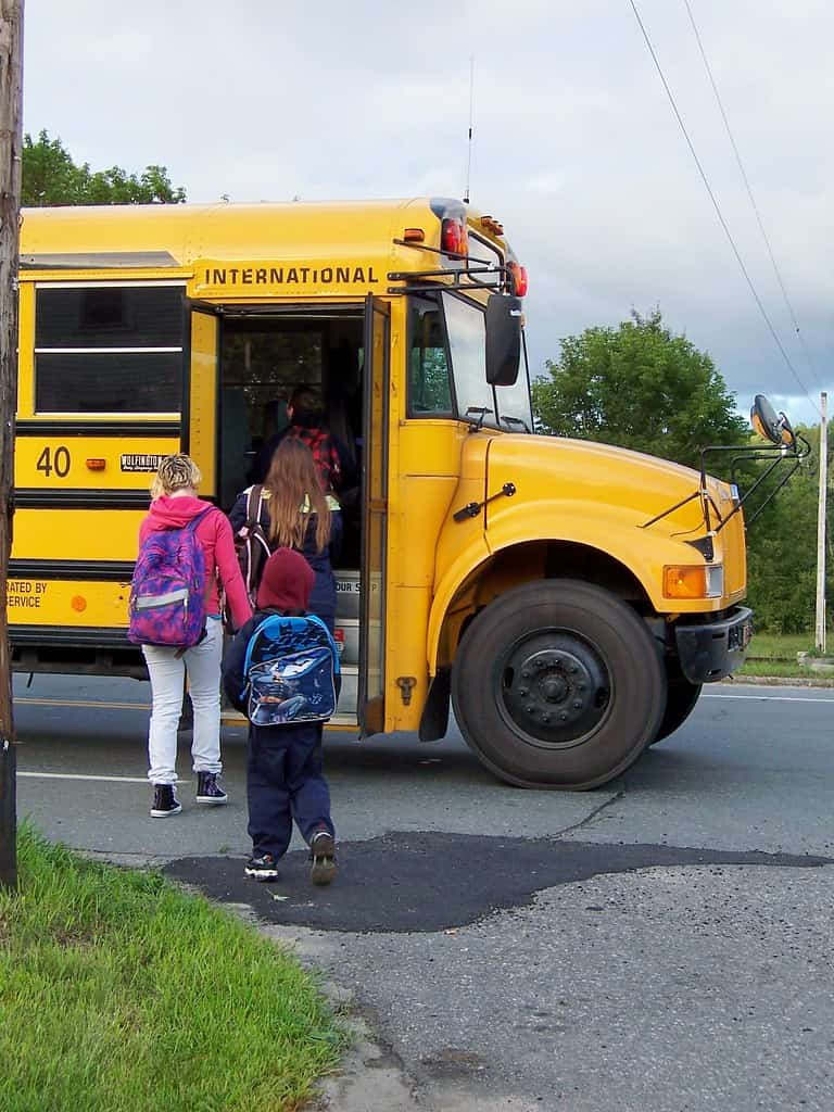 Students board a yellow school bus on the first day of school